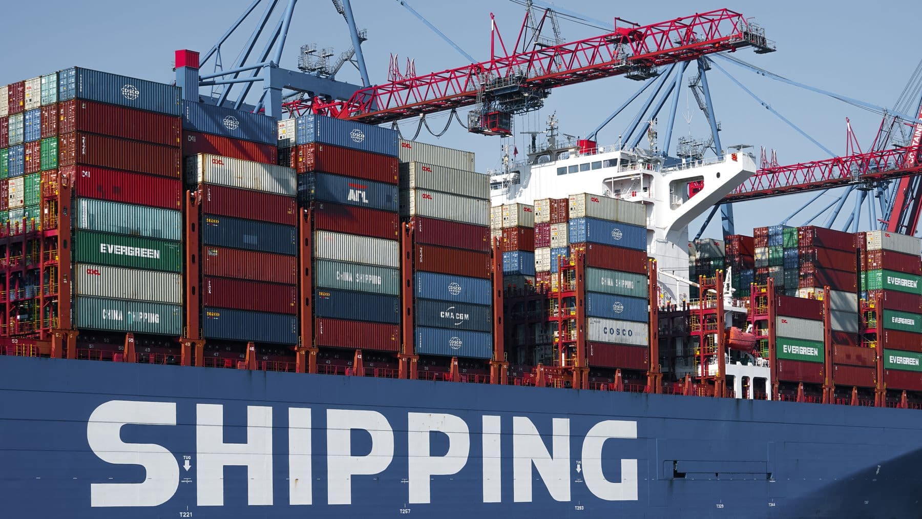 Gantry cranes working a container ship at a busy port terminal, containers stacked high on deck.